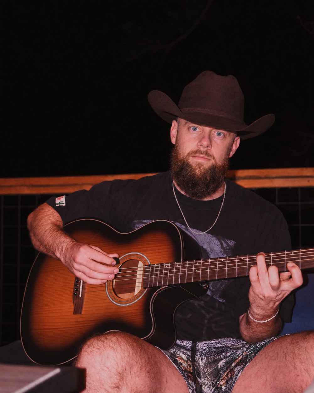 Colton Bushue in a cowboy hat, playing an acoustic guitar